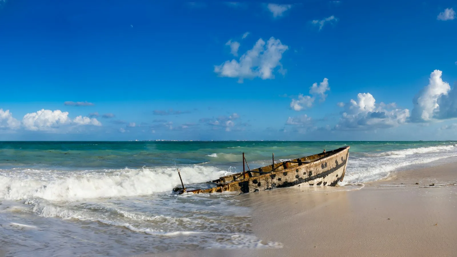 Barca de madera varada en la orilla de una playa de Costa Mujeres, con mar turquesa y cielo azul