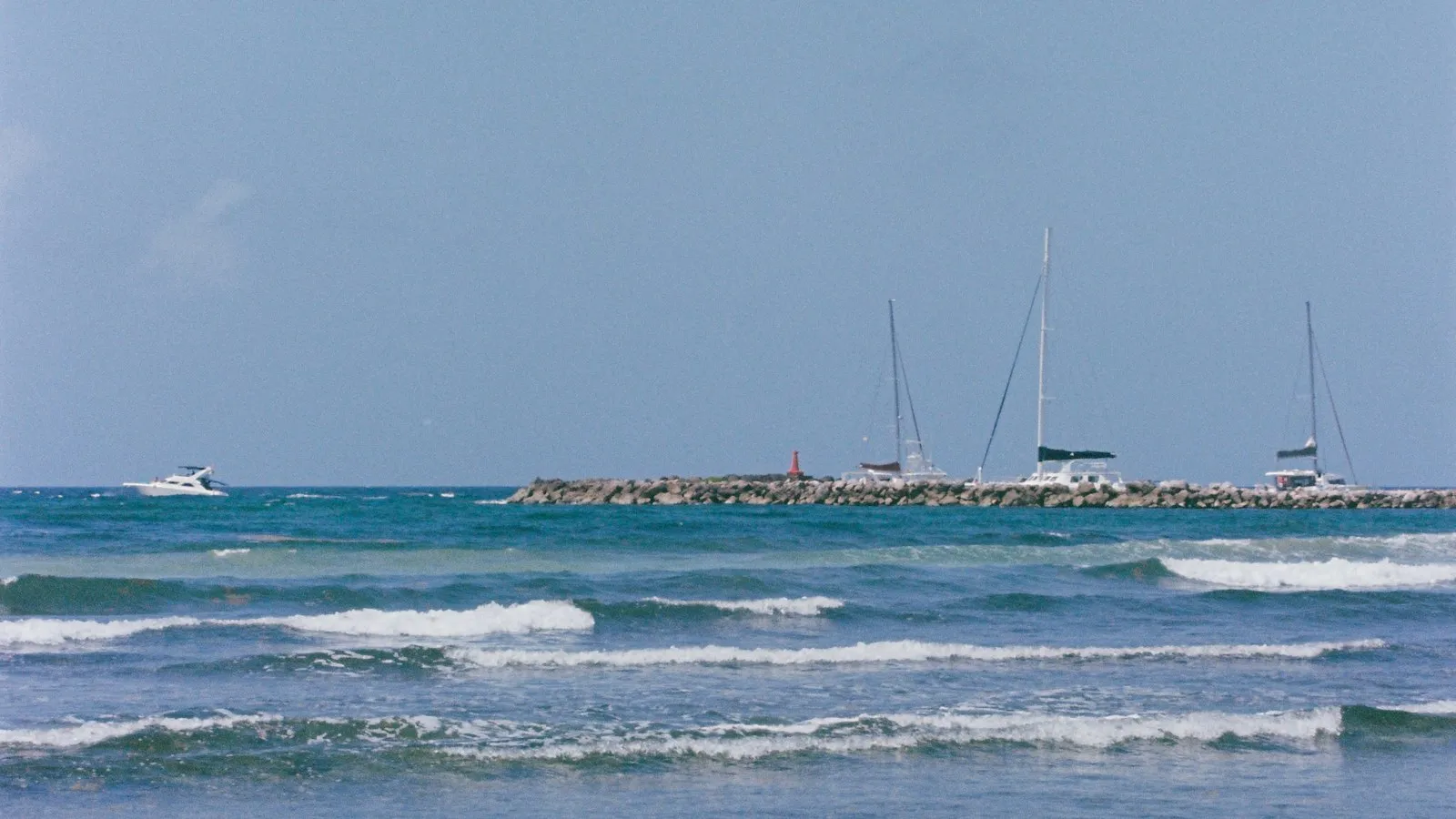 Veleros atracados tras el rompeolas de la marina de Puerto Aventuras, con olas en primer plano