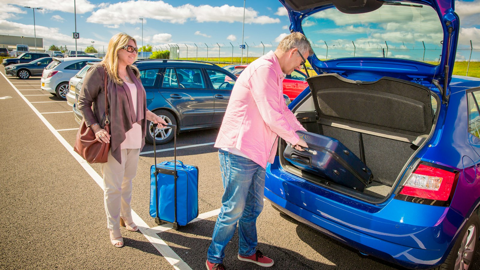 Pareja carga sus maletas en la cajuela de un auto en el estacionamiento del aeropuerto